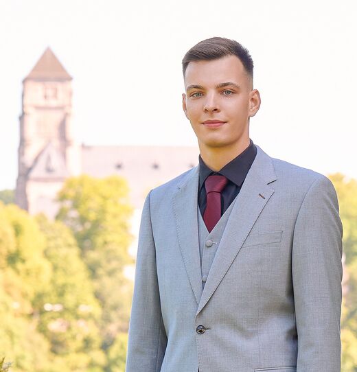 Porträt von Jimmy, Team von Pontura, im grauen Anzug vor einem Kirchturm